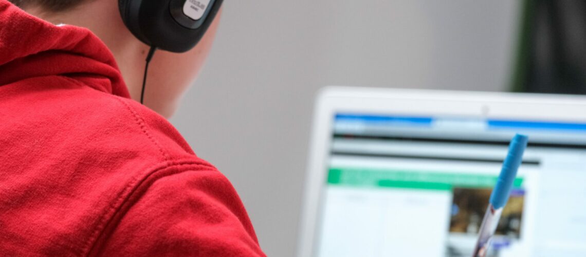 Person wearing a red sweater and headphone engaging in online learning